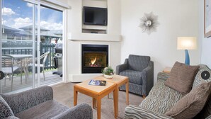 Ein Wohnzimmer mit Kamin, Fernseher und Blick ins Freie.