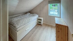 A small, single-bed room with a sloped ceiling, a window with a view of the outside, and a wooden dresser. - 2 bedroom beautiful home in Feda (Feda)