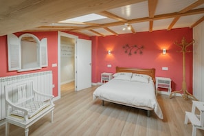 Ein Schlafzimmer mit einem Bett, einer Bank, einem Kleiderständer und einer Tür zu einem weiteren Raum.