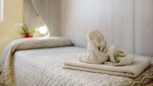 A neatly made bed with a folded towel and a blanket, a bedside table with a lamp, and a potted plant.