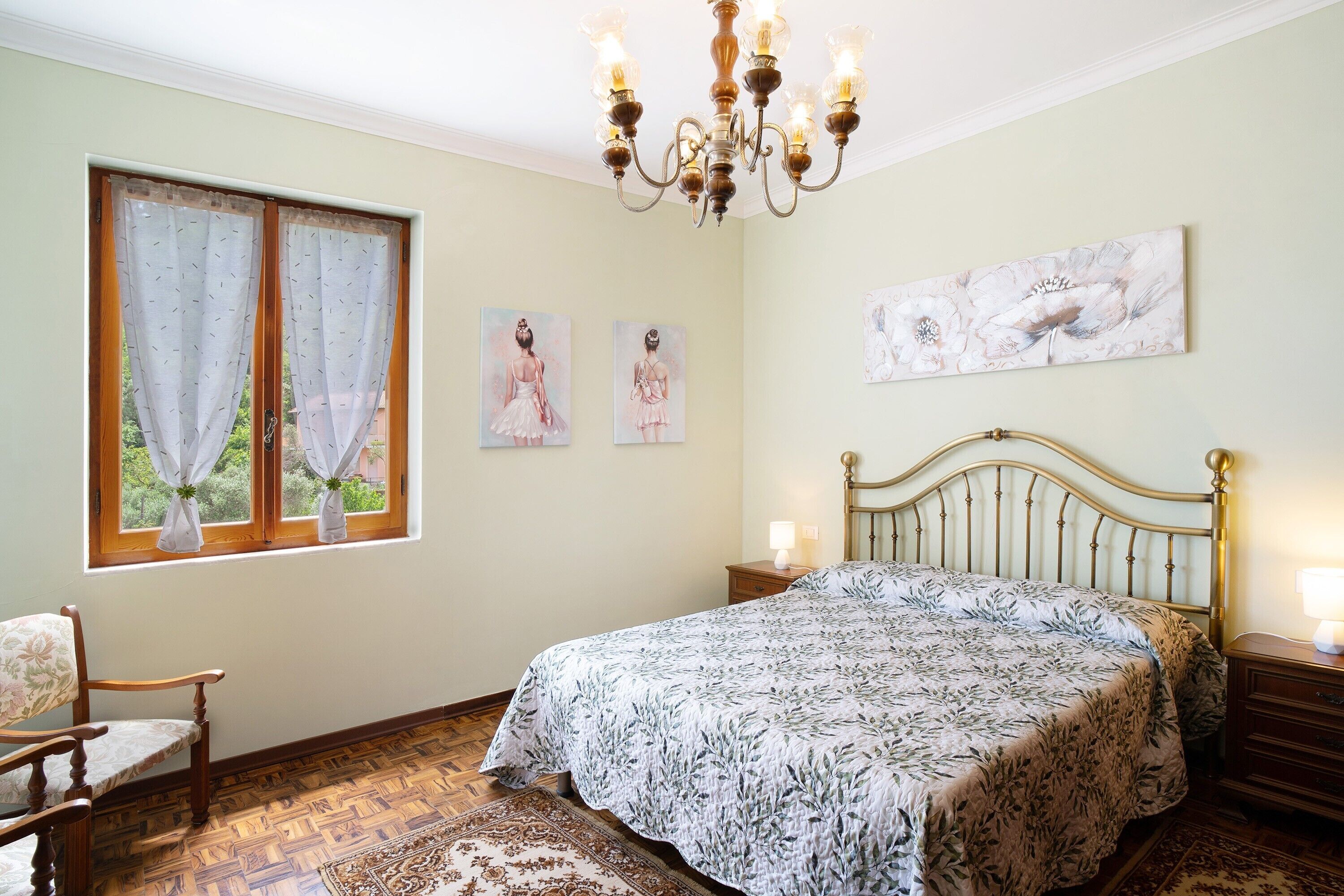 A bedroom with a bed, a chandelier, a window with curtains, and wall art.