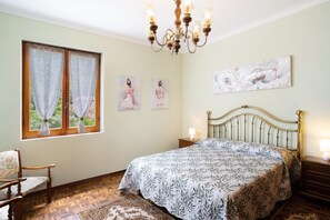 Une chambre à coucher avec un lit, un lustre, une fenêtre avec des rideaux et des œuvres d’art murales.