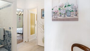 A hallway with a tiled floor, a door with a golden textured panel, and a painting of flowers on the wall.