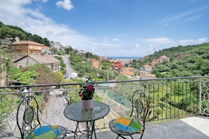 Un balcon avec une table et des chaises, un pot de fleurs et une vue sur une ville située sur une colline.