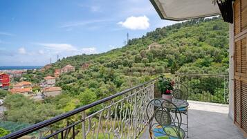 A balcony with a view of a hillside, a table with chairs, and a potted plant.