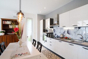 Une cuisine moderne avec des meubles blancs, un pare-feu en marbre et un coin repas avec une table dressée pour deux personnes.