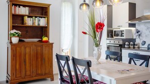 A dining area with a wooden cabinet, a vase with flowers, and a kitchen in the background.