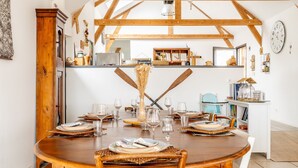 Comedor con mesa de madera dispuesta para cuatro personas, cocina al fondo y techo rústico.
