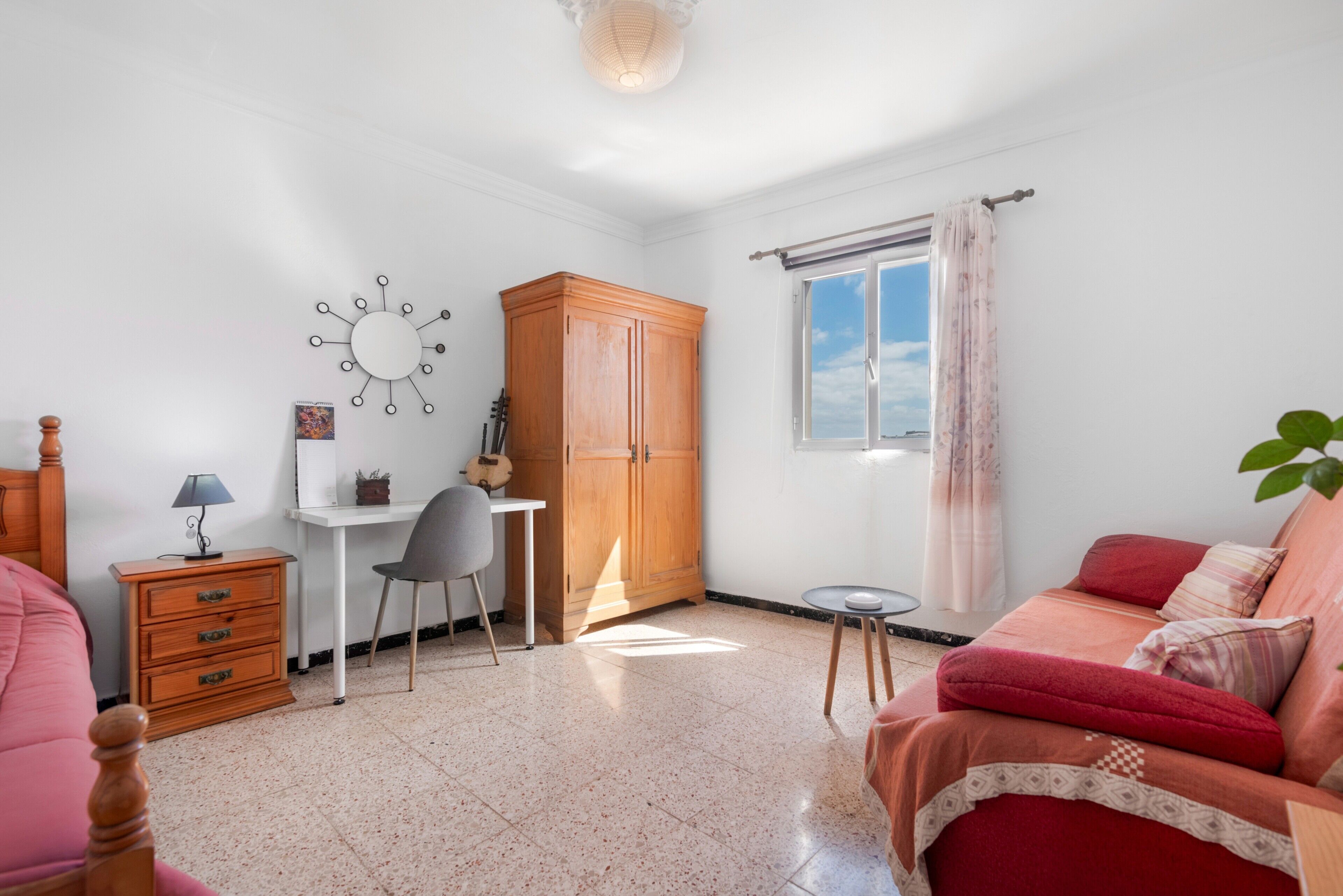 Ein Schlafzimmer mit Bett, Schreibtisch, Stuhl, Kleiderschrank und einem Fenster mit Vorhängen.