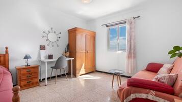 Ein Schlafzimmer mit Bett, Schreibtisch, Stuhl, Kleiderschrank und einem Fenster mit Vorhängen.