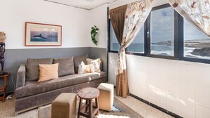 A living room with a sofa, a small round table, a window with curtains, a framed picture on the wall, and a plant. - Holiday Apartment 'Siempreviva' with Shared Pool and Wi-Fi (Gáldar)
