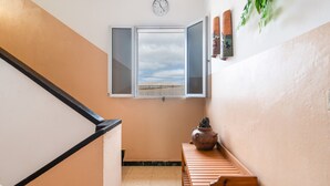 A staircase with a view of a greenhouse through an open window, a clock on the wall, and a wooden bench with a vase. - Holiday Apartment 'Siempreviva' with Shared Pool and Wi-Fi (Gáldar)