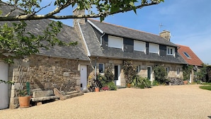 Une maison en pierre avec une allée en gravier, une cheminée et un petit jardin agrémenté de plantes en pot.