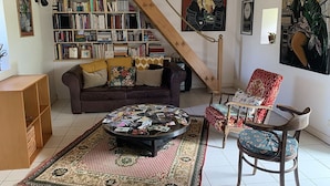 Un salon chaleureux avec un canapé marron, un tapis à motifs, une table basse avec des magazines, une bibliothèque et un escalier.