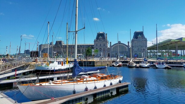 A marina with various boats docked, a large building with a distinctive arched entrance, and a covered area with a green roof. - Nice apartment in Oostende with WiFi (Oostende)