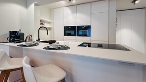 A modern kitchen with white cabinetry, a black faucet, and a built-in oven. There are two white bar stools and a coffee maker on the counter. - Nice apartment in Oostende with WiFi (Oostende)