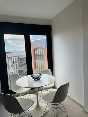 A modern dining area with a round table, two chairs, and a view of buildings through large windows.