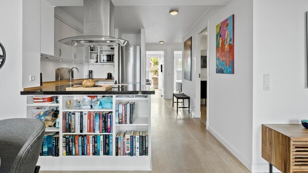 A modern kitchen with a central island, a bookshelf filled with books, and a dining area with a wooden table and chairs.