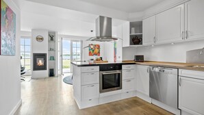 A modern kitchen with white cabinetry, a central island, stainless steel appliances, and a view to the outdoors.