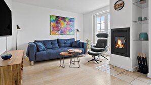 A modern living room with a blue sofa, a round coffee table, a black leather chair, a fireplace, and a colorful abstract painting on the wall.