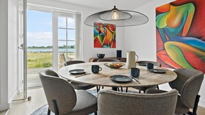 A dining area with a round table, chairs, a hanging light fixture, and a large abstract painting.
