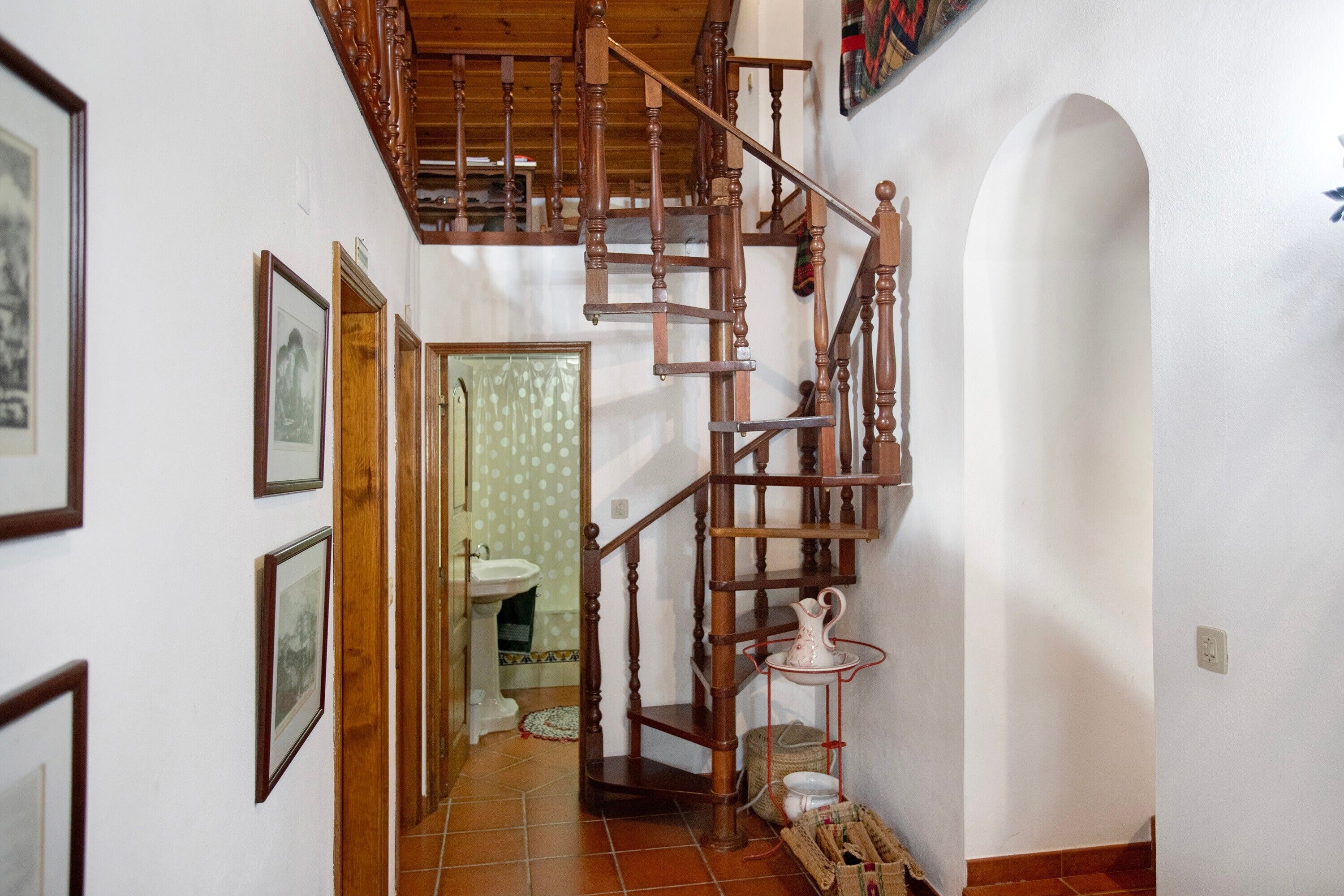 Una escalera de madera que sube a un piso superior, un lavamanos y cuadros enmarcados en las paredes.
