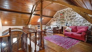 Un espai tipus loft amb una escala de fusta, paret de pedra i un sofà vermell.