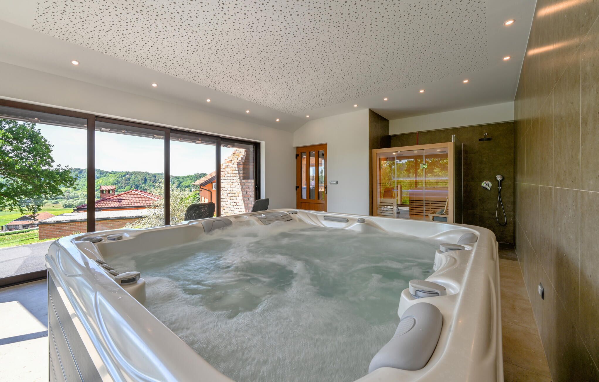 Un baño moderno con un jacuzzi grande, un box de ducha de cristal y vistas al campo.