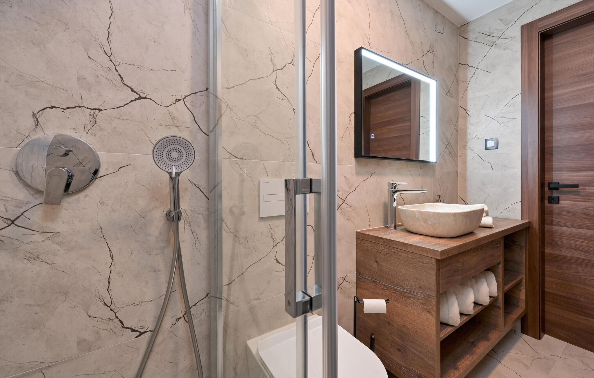 Un bagno moderno con box doccia in vetro, parete rivestita in marmo, mobile lavabo in legno e uno specchio grande.