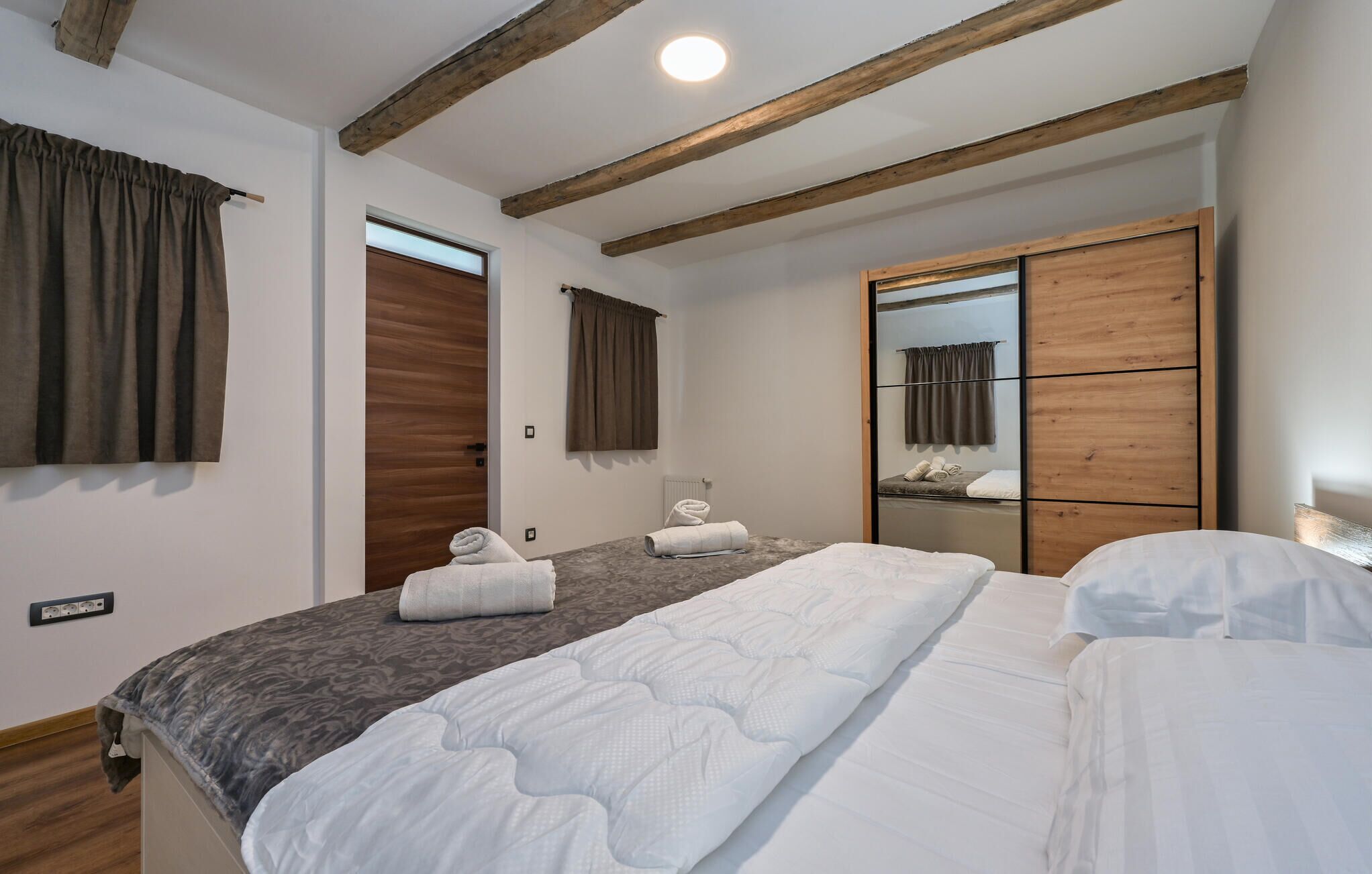 A hotel room with a large bed, a wooden wardrobe, a mirror, and a window with curtains.
