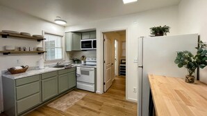 A modern kitchen with light wood flooring, white cabinets, a built-in microwave, and a refrigerator. - The Birch at Lazy Oaks Resort (duplex) (Lakeside)