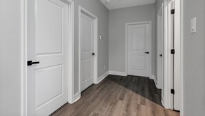 A hallway with white doors, a wooden floor, and a ceiling with recessed lighting.