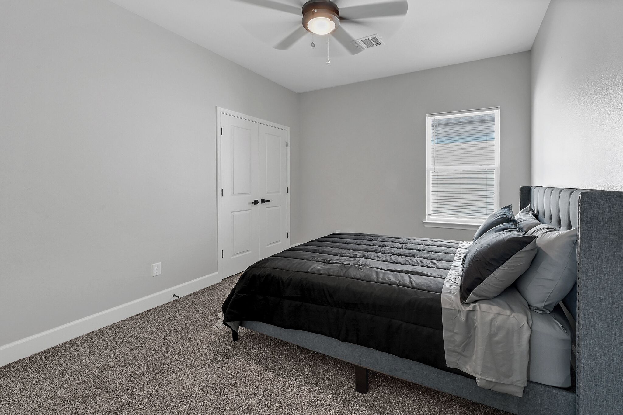 A bedroom with a bed, a ceiling fan, a window with blinds, and a door.