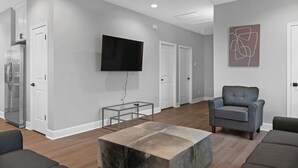 A modern living room with a flat-screen TV, a grey armchair, a coffee table, and a refrigerator.