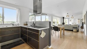 Una cocina moderna con una isla central, un comedor con mesa y sillas, y una sala de estar con sofá y chimenea.