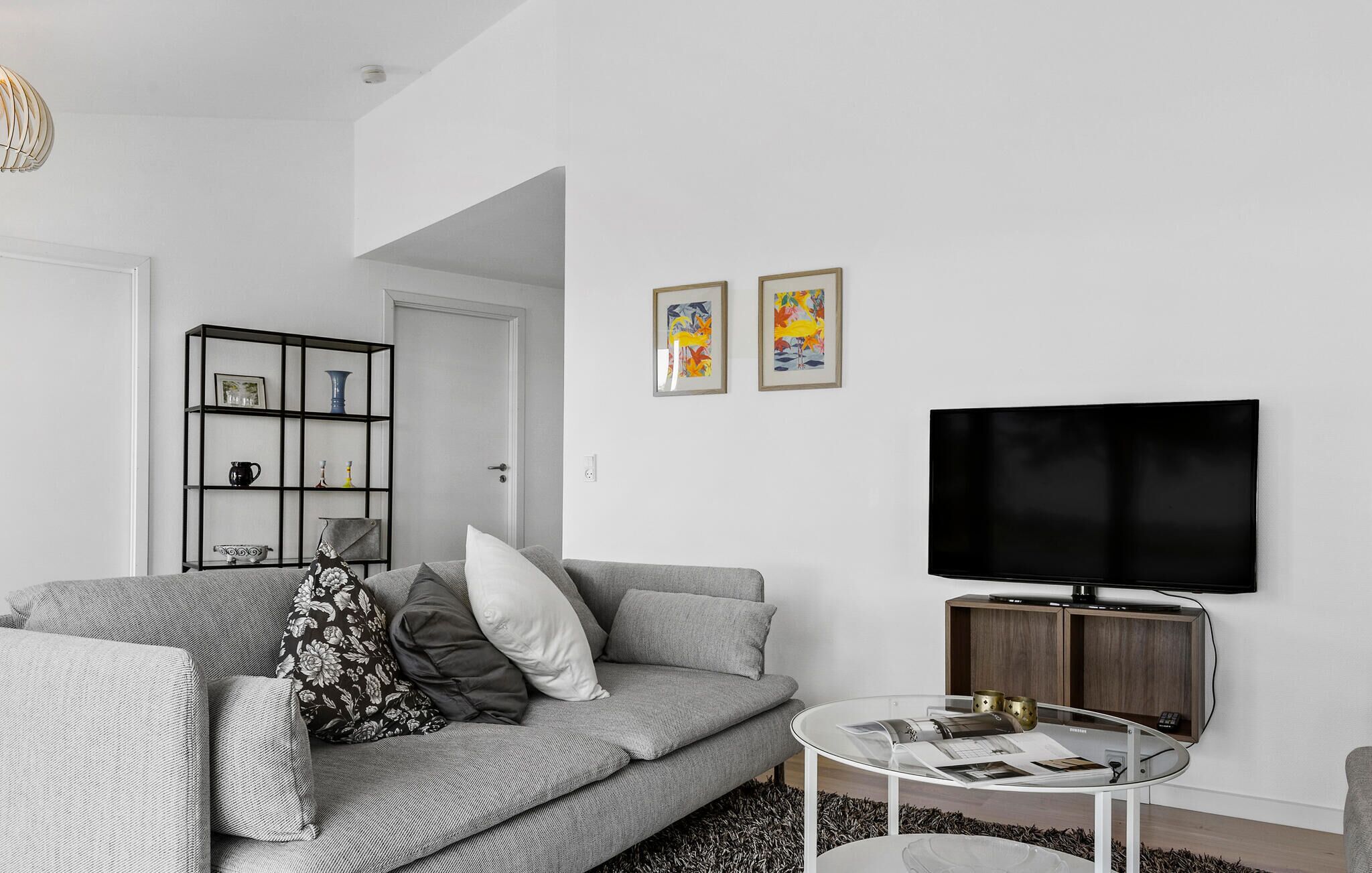 A modern living room with a grey sofa, a black TV, and a glass coffee table.