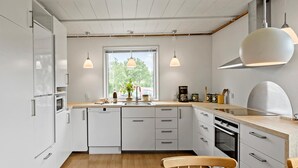 Una cucina moderna con mobili bianchi, un piano di lavoro in legno e illuminazione a sospensione.
