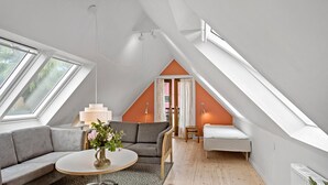 Una camera da letto moderna mansardata con soffitto spiovente, ampie finestre, un divano grigio, un tavolino con un vaso e un letto singolo.