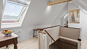 Una stanza con soffitto spiovente, un tavolo di legno con frutta, una scala con ringhiera in legno e un quadro appeso al muro.