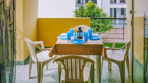 Un balcon avec une table dressée pour deux personnes, agrémenté de chaises en plastique blanc et d’une nappe.