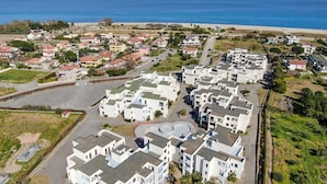 Vue aérienne d’un quartier résidentiel situé sur la côte, avec des bâtiments modernes blancs, un rond-point central et une plage en arrière-plan.