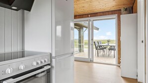 A modern kitchen with a built-in oven and stove, a wooden ceiling, and a sliding glass door leading to an outdoor patio with a table and chairs.