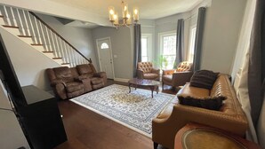 A spacious living room with a staircase, leather sofas, a coffee table, and a chandelier.
