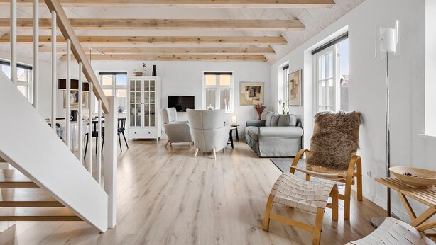 A spacious living area with a wooden staircase, a dining area with a table and chairs, and a seating area with sofas and a chair.