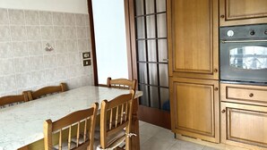 A dining area with a marble table and wooden chairs, a wooden cabinet with a built-in oven, and a tiled backsplash. - SE090 - Marzocca, comfortable three-room apartment 150 meters from the sea (Marzocca)