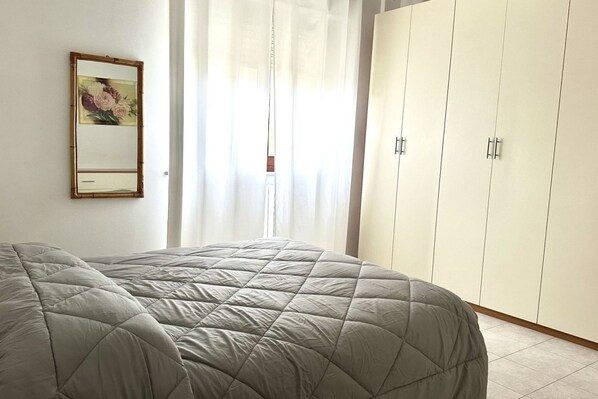 A bedroom with a bed, a wardrobe, a mirror, and a window with curtains.