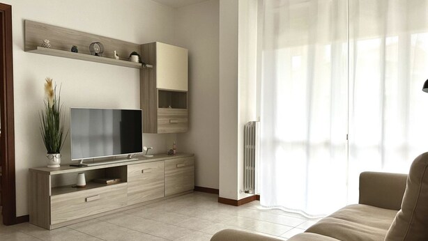 A modern living room with a flat-screen TV, light wood furniture, a beige sofa, and a large window with sheer curtains. - SE090 - Marzocca, comfortable three-room apartment 150 meters from the sea (Marzocca)