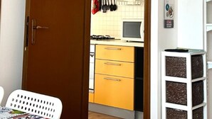 Een keuken met een magnetron, een fornuis en een spoelbak. Er zijn kastjes en een witte stoel.