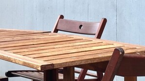 Een houten tafel met vier stoelen, geplaatst tegen een effen muur.