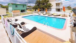 A rectangular swimming pool with a wooden deck, surrounded by lounge chairs and umbrellas, with a white fence and houses in the background. - Seabirds Motel At Kure Beach (Kure Beach)